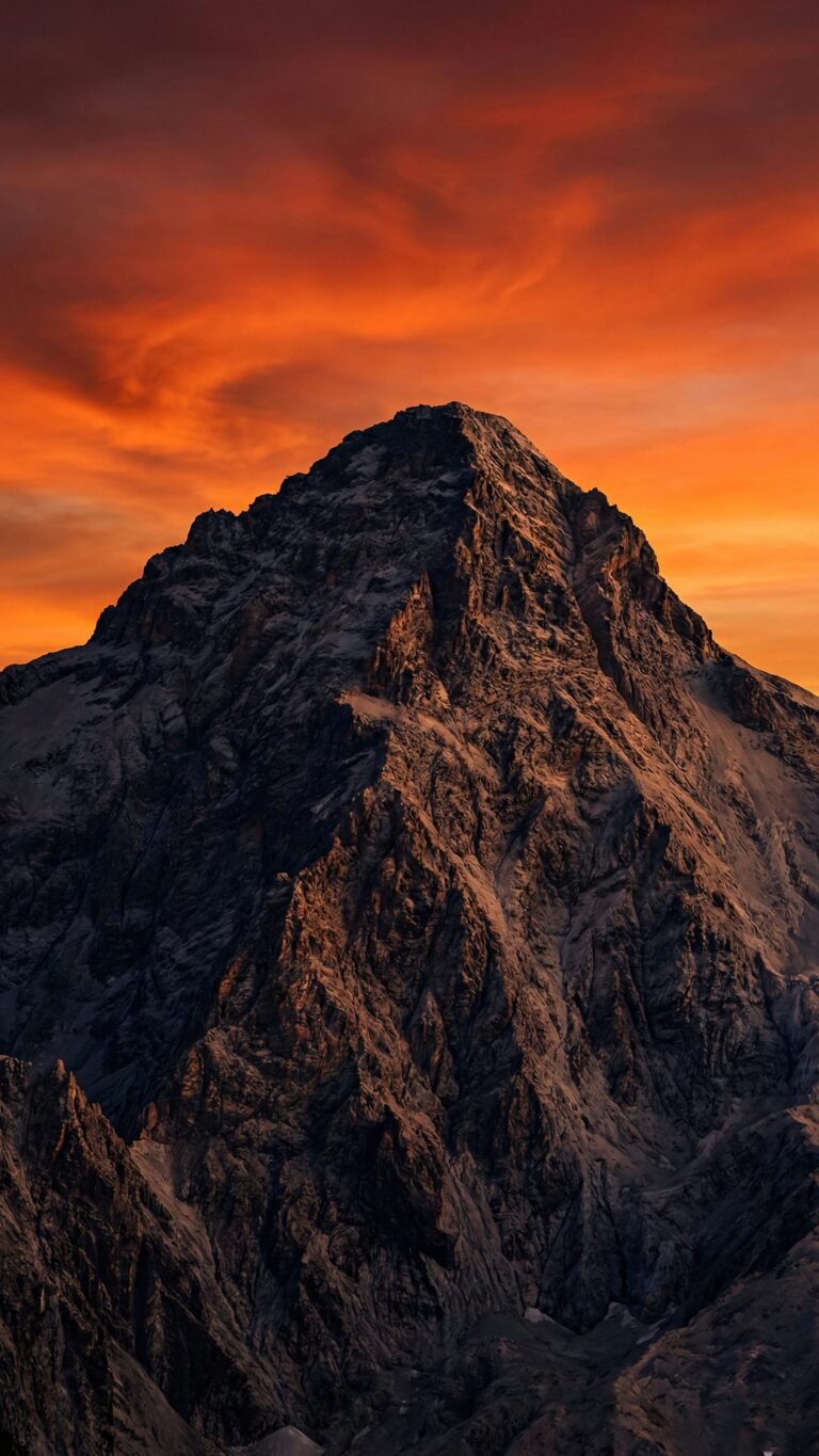 Highly detailed digital render of a majestic rugged mountain peak set against a dramatic fiery orange and red sunset sky aesthetic 4K ultra HD mobile wallpaper