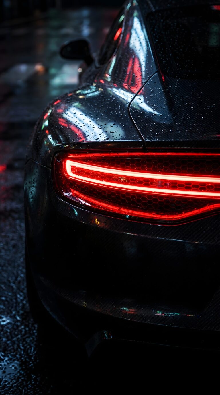 Close up of a dark sports car with glowing red taillight and wet rain drops on paint aesthetic 4K ultra HD mobile wallpaper
