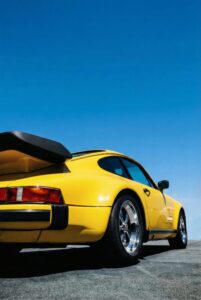 Side view of a vibrant yellow classic sports car on a sunny road with blue sky background