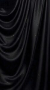 Close-up of black wavy silk fabric with golden glitter particles in a dark void.