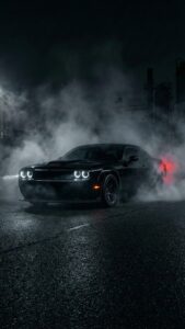 Vertical automotive photography of a pitch black Dodge Challenger muscle car emerging from thick white smoke at night, halo ring headlights glowing, industrial background, wet asphalt road, moody dark aesthetic 4K wallpaper