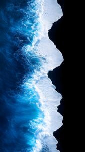 Vertical aerial drone photography of deep blue ocean waves with bright white sea foam crashing onto a pitch-black volcanic sand beach, high contrast nature background, minimalist coastal aesthetic 4K wallpaper