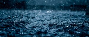 Panoramic ultra-wide photography of heavy rain drops falling on a dark blue water surface, creating splashes and ripples, cinematic bokeh effect, moody deep blue aesthetic, 4K desktop background