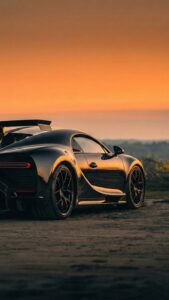 Vertical automotive photography of a black Bugatti Chiron hypercar parked on a dirt road during sunset, golden hour lighting reflecting on the car's curves, rear profile view, luxury lifestyle aesthetic 4K wallpaper
