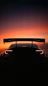 Vertical automotive photography, silhouette of a modified sports car (Subaru BRZ / Toyota GT86 style) rear view with large GT wing spoiler, glowing C-shaped taillights, vibrant orange and purple sunset sky background, JDM tuner aesthetic 4K wallpaper
