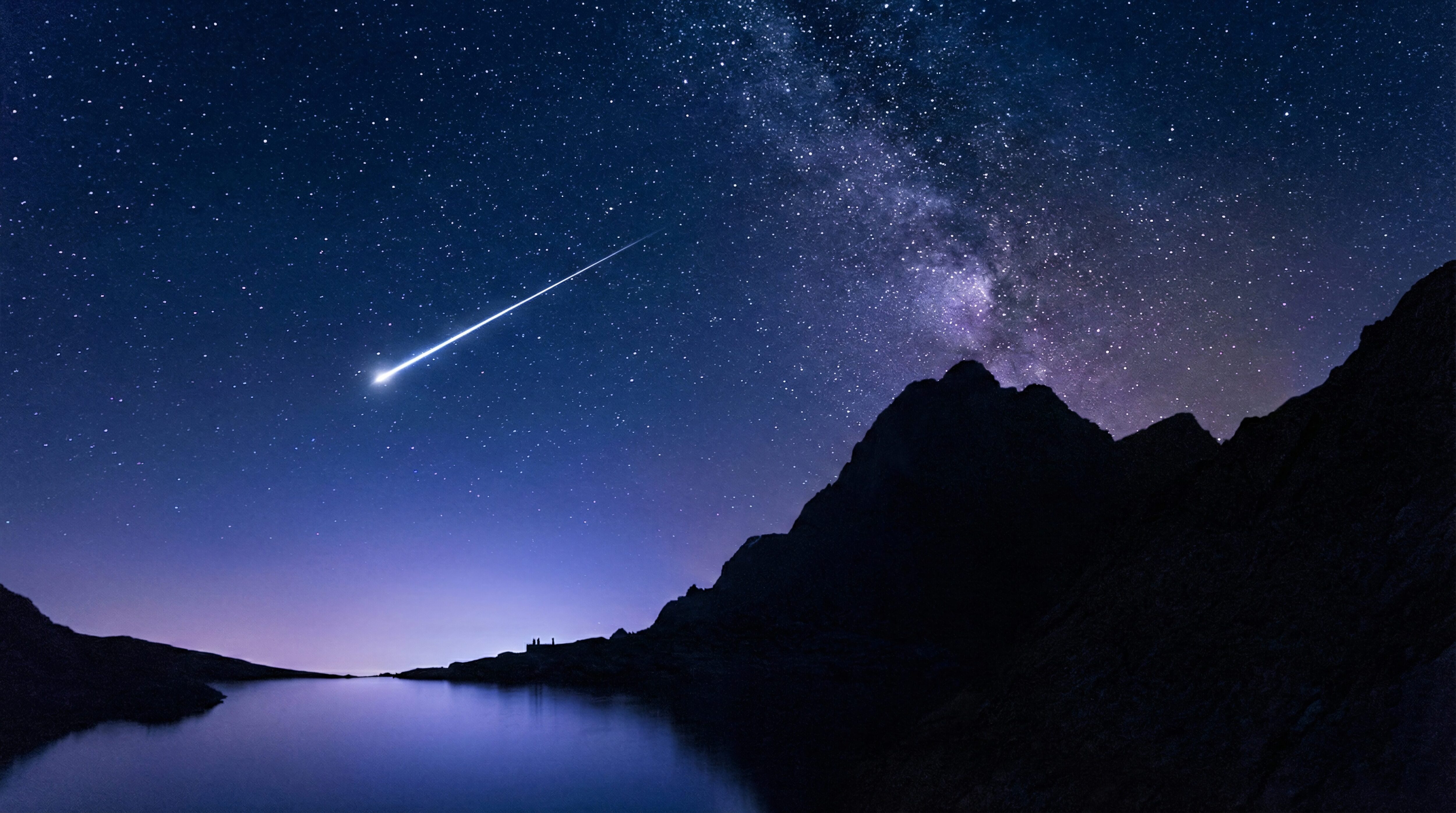Landscape night photography featuring a bright shooting star streaking across a deep blue starry sky with the Milky Way, positioned above a silhouette of jagged mountains and a calm lake reflection, 4K desktop wallpaper.