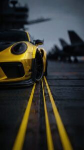 Vertical cinematic shot of a bright yellow Porsche 911 GT3 RS parked on a wet aircraft carrier flight deck, blurry fighter jet silhouettes in the background, yellow runway lines leading to the car, moody dark grey sky, 4K automotive wallpaper