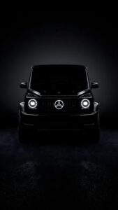 Highly detailed digital render of a sleek black Mercedes Benz G-Wagon luxury SUV with glowing circular LED headlights and illuminated star logo parked in a pitch black dark studio setting mafia automotive aesthetic 4K ultra HD mobile wallpaper