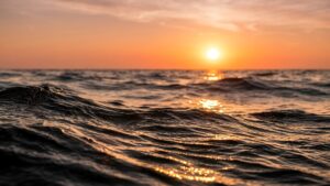 Highly detailed 4K digital photography of warm golden sunset light reflecting on rolling dark ocean waves, optimized as a cool desktop wallpaper.
