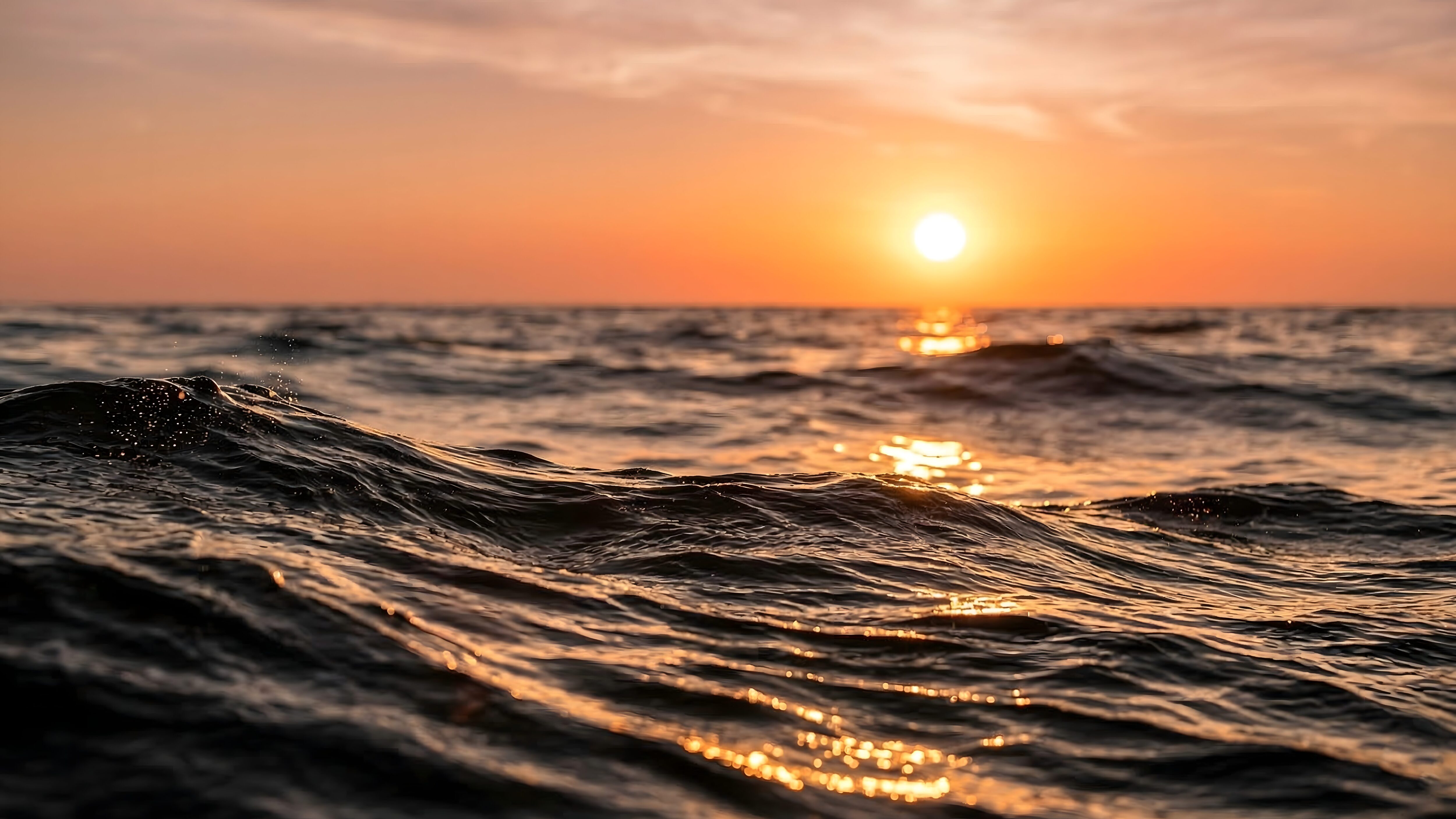 Highly detailed 4K digital photography of warm golden sunset light reflecting on rolling dark ocean waves, optimized as a cool desktop wallpaper.