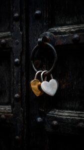 Highly detailed 4K photography of gold and silver heart-shaped padlocks hanging from an iron ring on a rustic dark wooden door, optimized as cool black wallpaper art for phone.