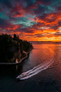 Highly detailed digital render of a luxury yacht sailing on the ocean near a rocky coastal cliff with a lighthouse under a dramatic fiery sunset aesthetic 4K ultra HD mobile wallpaper
