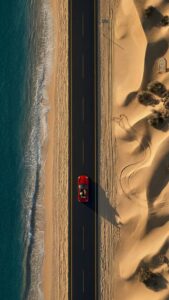 Highly detailed 4K aerial drone photography of a red convertible car driving on a straight road between a beautiful blue ocean beach and golden desert sand dunes, optimized as cool wallpaper art for phone.
