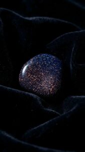 Highly detailed 4K wallpaper featuring a polished, sparkling obsidian gemstone resting gracefully on folded deep black velvet fabric, creating a deeply luxurious and dark minimalist background.