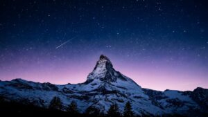 Highly detailed digital landscape photography of a majestic snow-capped mountain peak under a magical starry night sky featuring a shooting star and purple horizon aesthetic 4K ultra HD PC desktop wallpaper
