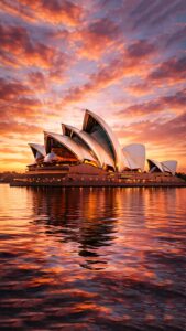 Highly detailed 4K wallpaper featuring the iconic Sydney Opera House glowing under a breathtaking golden sunset, with perfect warm reflections on the calm harbor water.