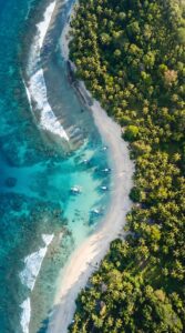 Tropical Beach Aerial Wallpaper 4K, stunning drone view digital art of turquoise ocean water, white sand beach, small boats, and dense green palm trees.