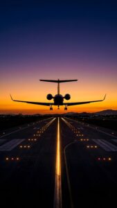 A high-resolution 4K mobile wallpaper featuring the silhouette of a private jet landing on a glowing runway during a vibrant purple and orange sunset.