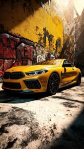 A high-resolution 4K mobile wallpaper of a bright yellow BMW M8 Competition parked in an urban alley with colorful graffiti on a brick wall.