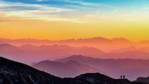 Vibrant 4K desktop wallpaper of colorful misty mountains during sunset with silhouettes of two hikers on a ridge.