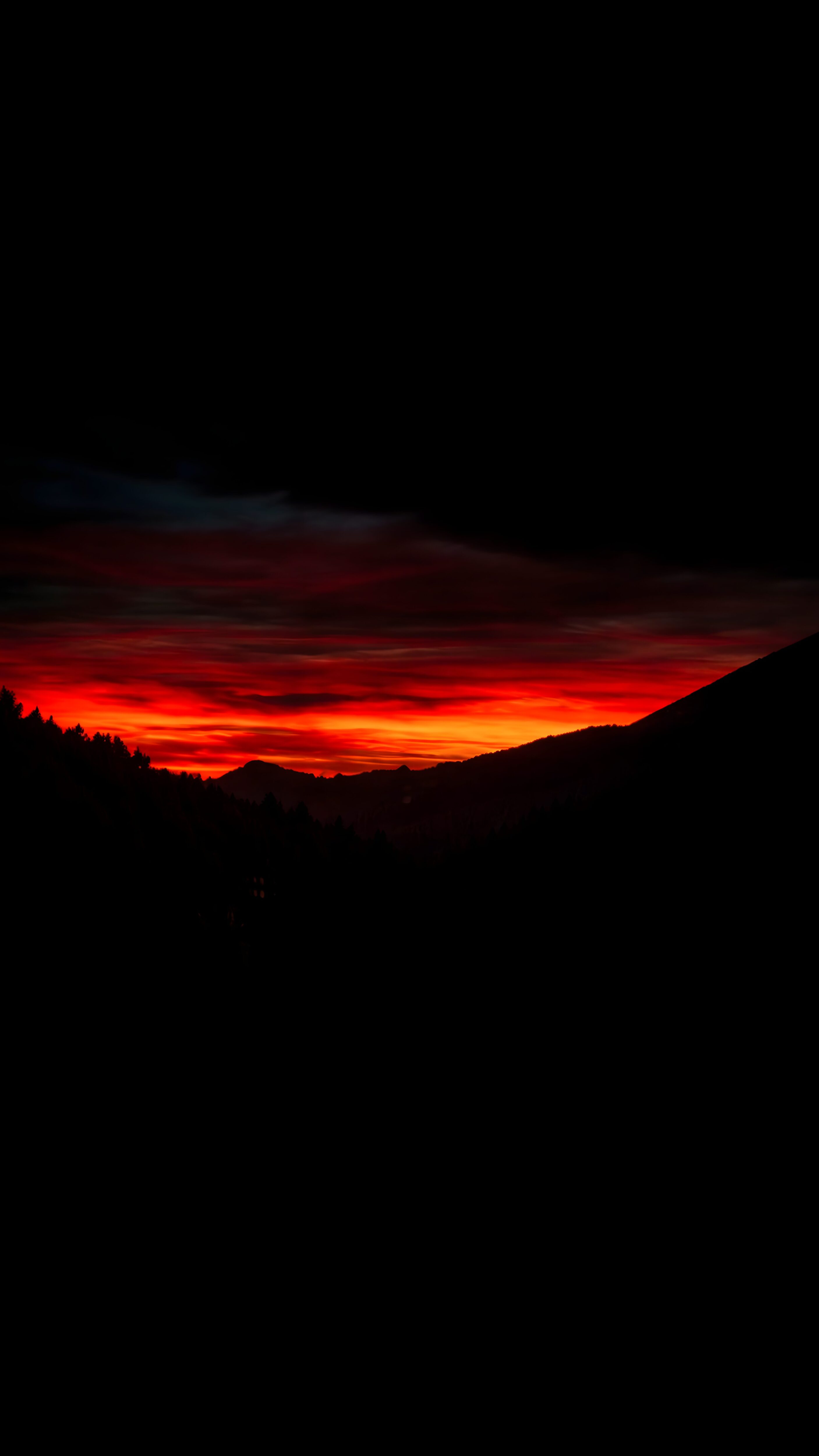 A 4K AMOLED mobile wallpaper featuring a bright red and orange sunset glowing between a completely pitch black sky at the top and black mountain silhouettes at the bottom.