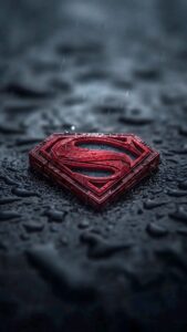 A high-resolution 4K mobile wallpaper of a textured, metallic red Superman logo resting on a dark, wet surface covered in raindrops.