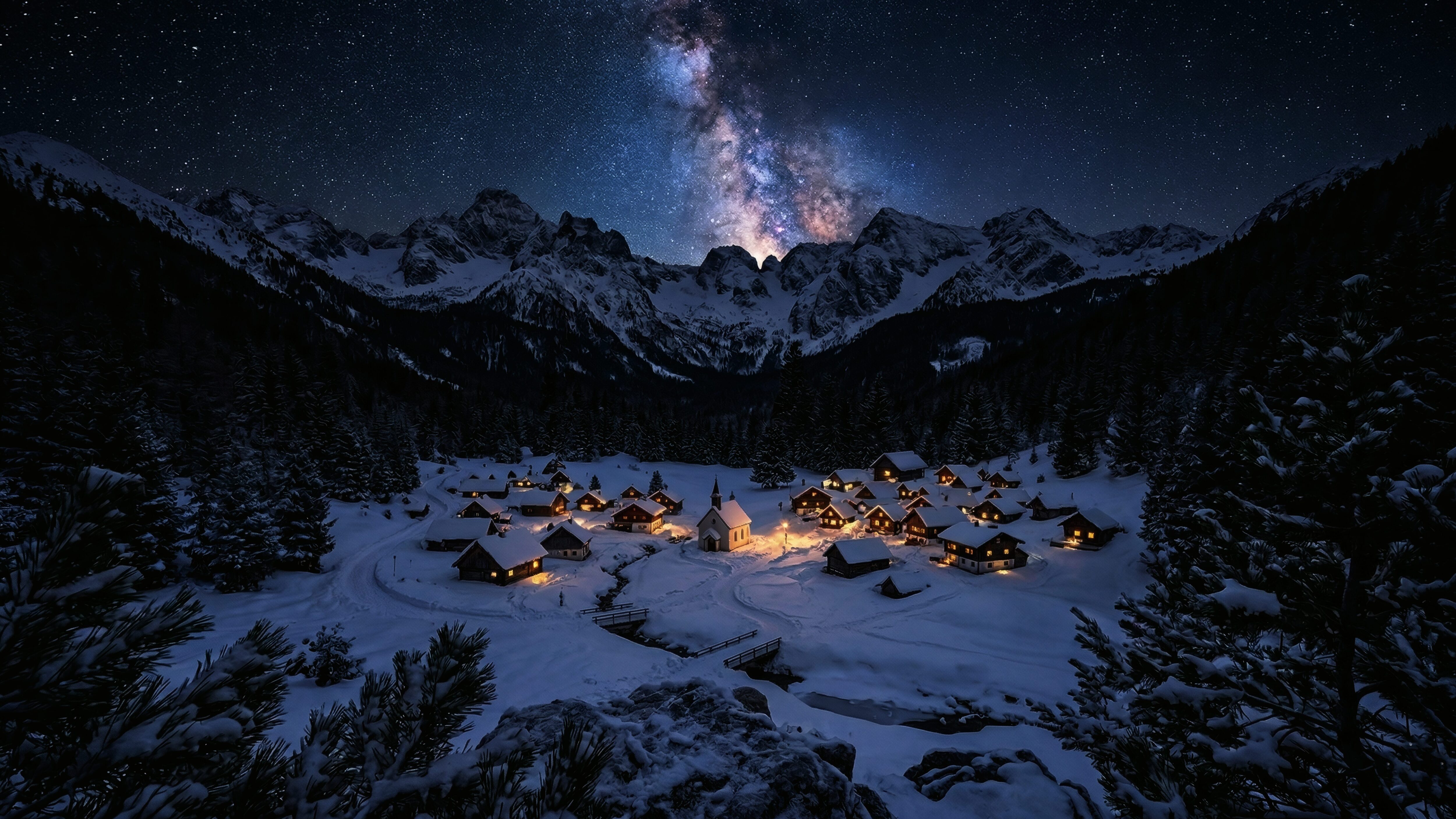 A high-resolution 4K desktop wallpaper of a small village in a snowy mountain valley with warm glowing lights under the Milky Way galaxy.