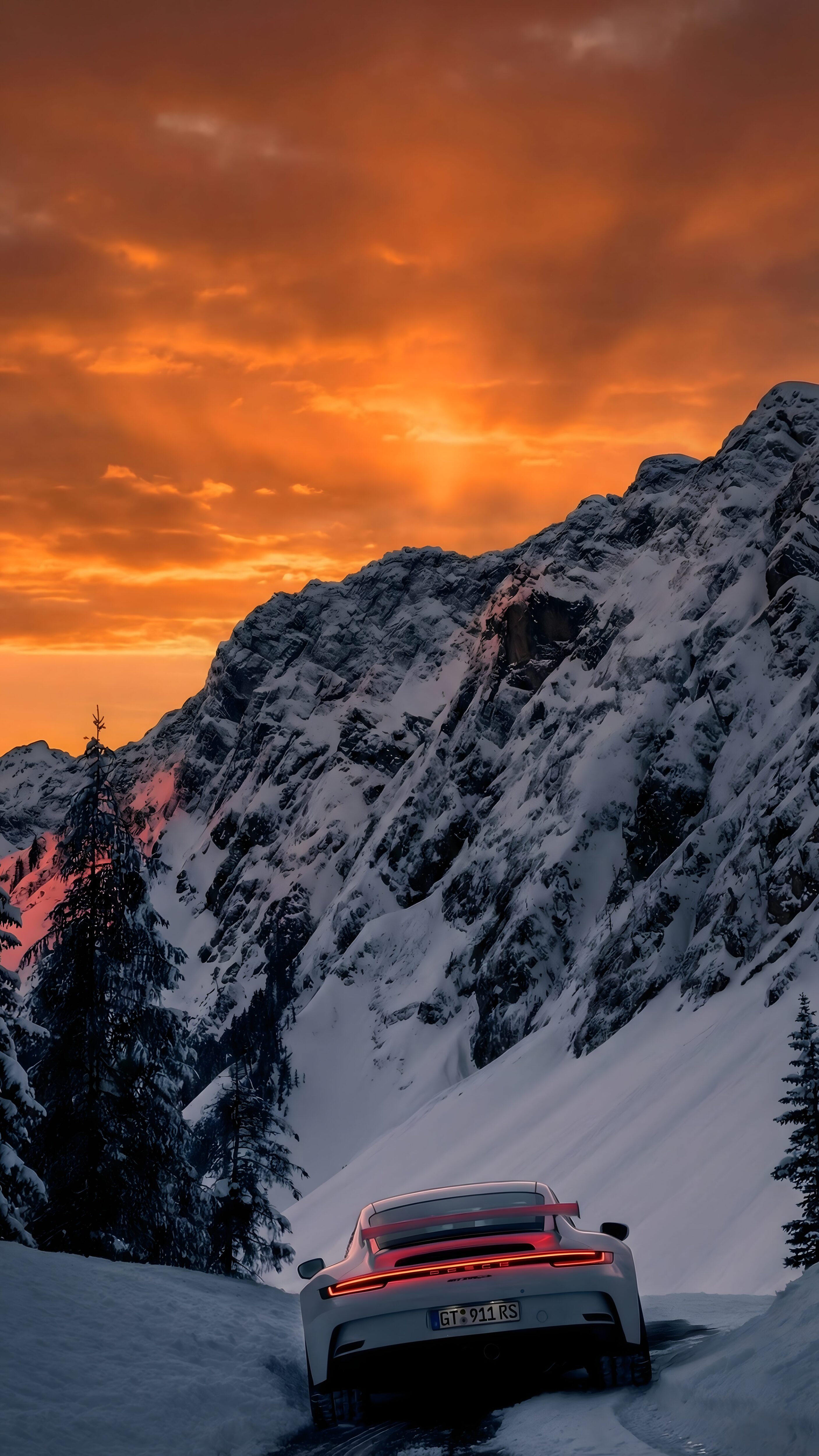 A high-resolution 4K mobile wallpaper of a white Porsche 911 GT3 RS on a snowy mountain road with a vibrant orange sunset sky in the background.