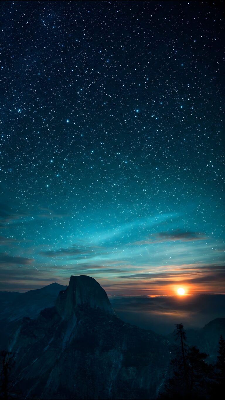 A high-resolution 4K iPhone wallpaper featuring the dark silhouette of a mountain peak against a vast starry night sky that transitions into a glowing orange sunrise.
