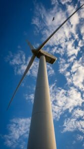 Sharp 4K mobile wallpaper of a tall wind turbine reaching into a bright blue sky with white clouds and a bird flying above.