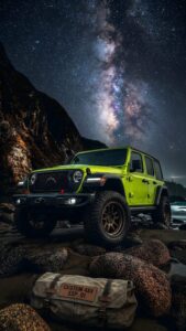 Bright green custom 4x4 off-road vehicle parked on rocky terrain under a spectacular Milky Way night sky.