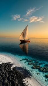 A traditional sailboat gliding on calm turquoise water over coral reefs, viewed from a beach with striking black and white sand under a sunset sky.