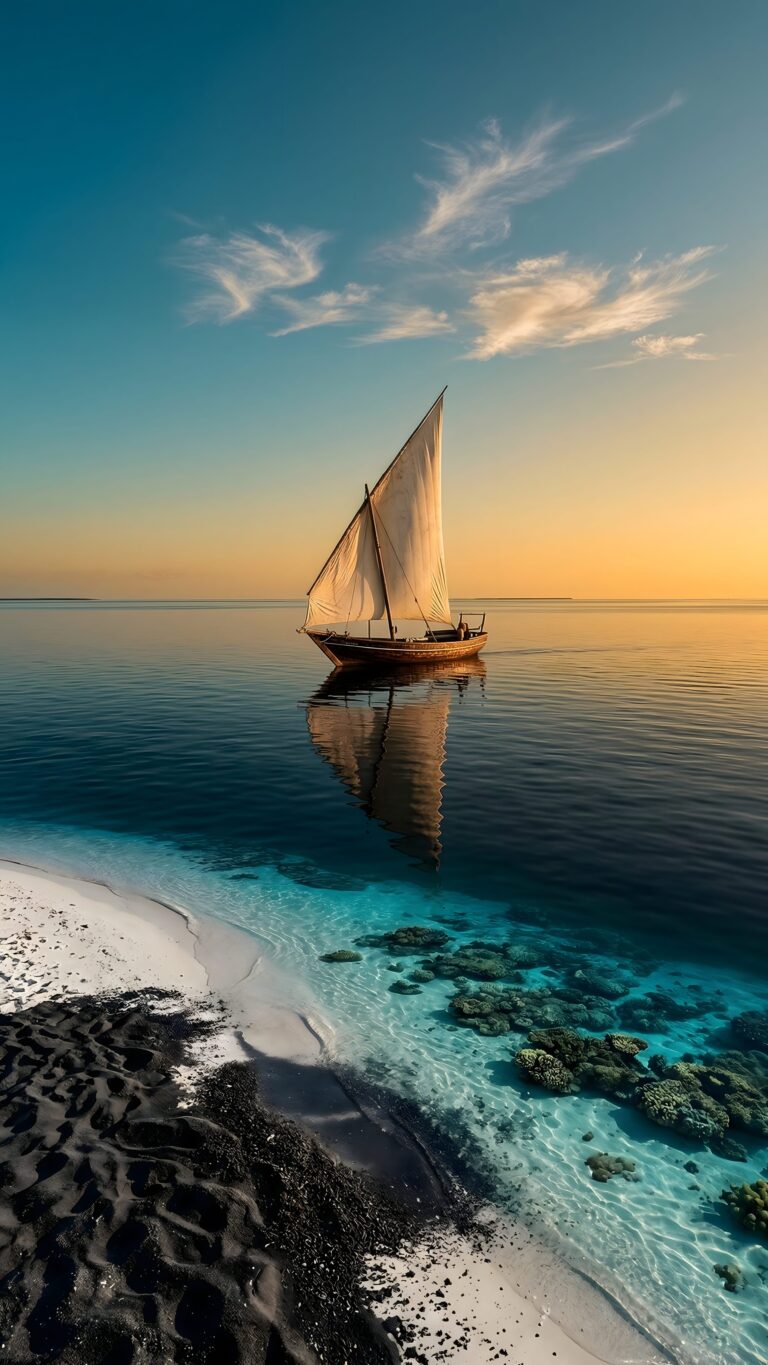 A traditional sailboat gliding on calm turquoise water over coral reefs, viewed from a beach with striking black and white sand under a sunset sky.