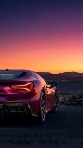 Magenta sports car parked by the water during a vibrant purple and orange sunset.