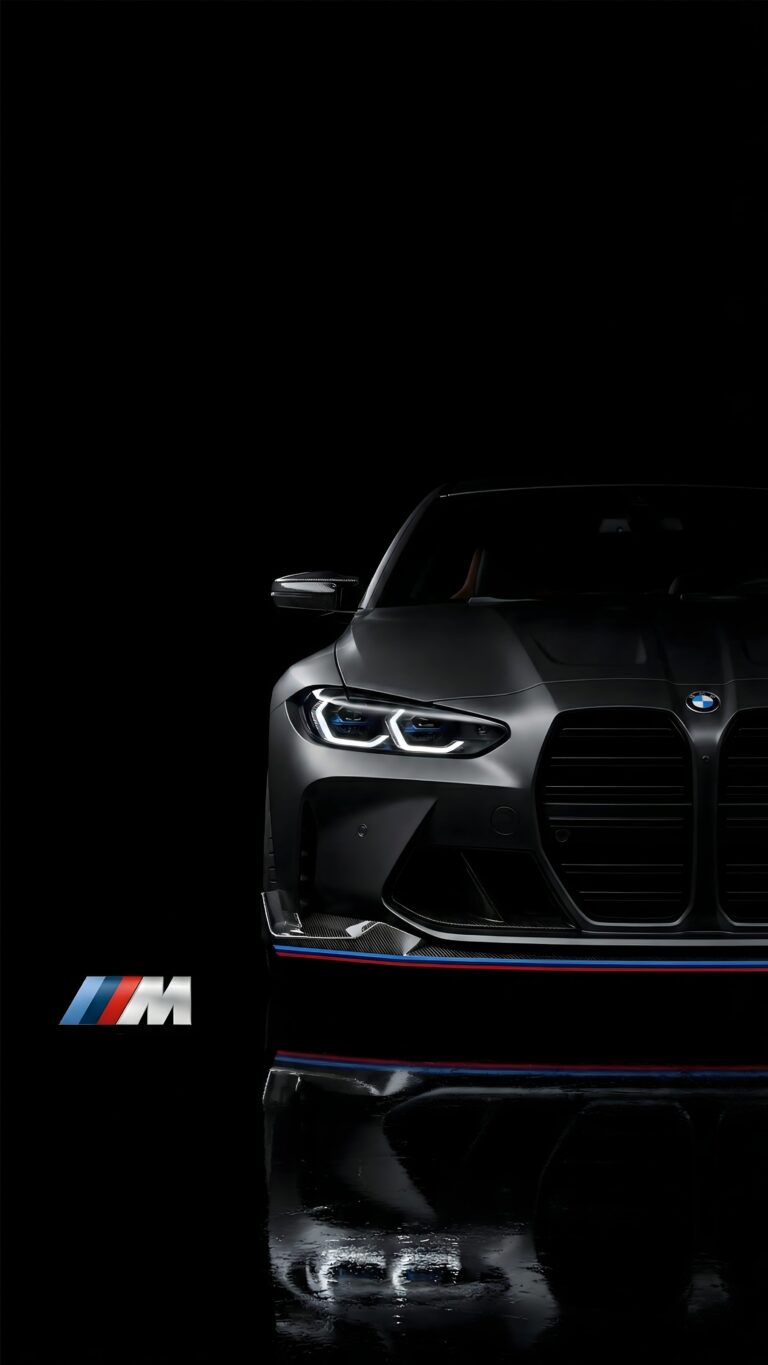 Front view of a sleek matte black BMW M series car with illuminated headlights and an M logo reflection on a pitch-black background.