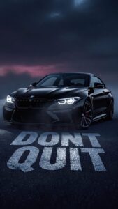 A sleek black BMW sports car parked on asphalt with the motivational phrase DONT QUIT painted on the ground under a dark, moody twilight sky.