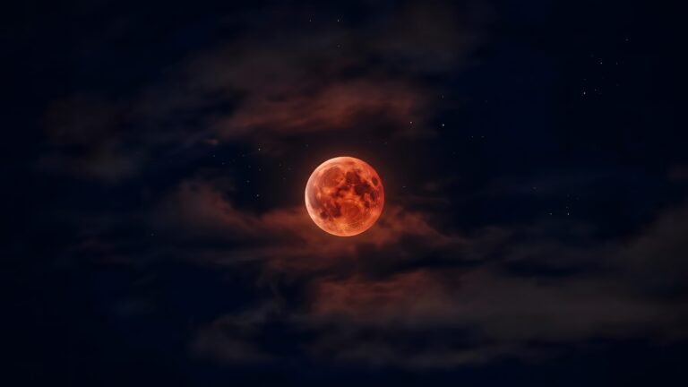 A glowing, intricately textured red blood moon surrounded by dramatic dark clouds and faint stars in a night sky.