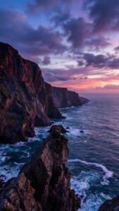 Dramatic coastal cliffs overlooking a crashing blue ocean under a purple and pink sunset sky.