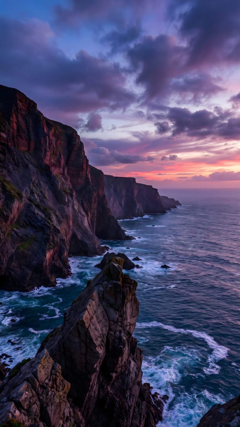 Dramatic coastal cliffs overlooking a crashing blue ocean under a purple and pink sunset sky.