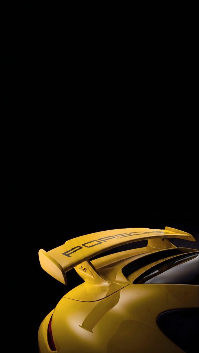 Close-up detail of a bright yellow Porsche 3.8 rear wing against a pitch-black background.