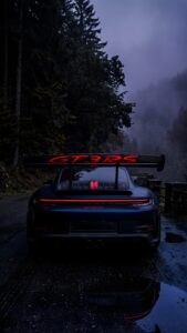 Dark grey Porsche GT3 RS parked on a wet, misty forest road with glowing red taillights, optimized for mobile screens.