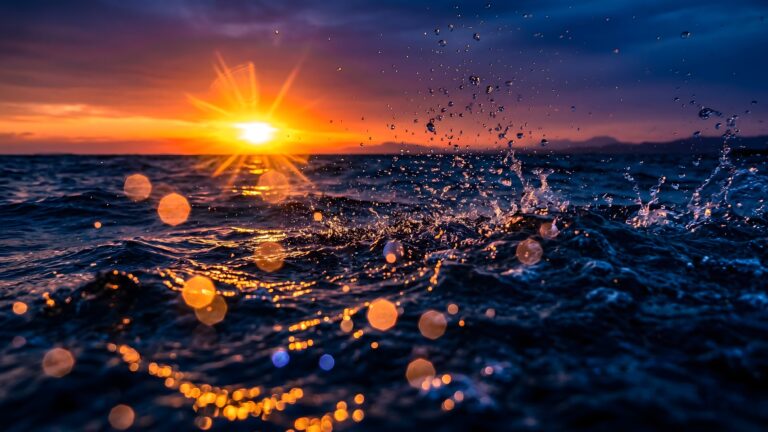 A dramatic sunset over a dark blue ocean with dynamic water splashing in the foreground and golden bokeh lights reflecting on the waves.