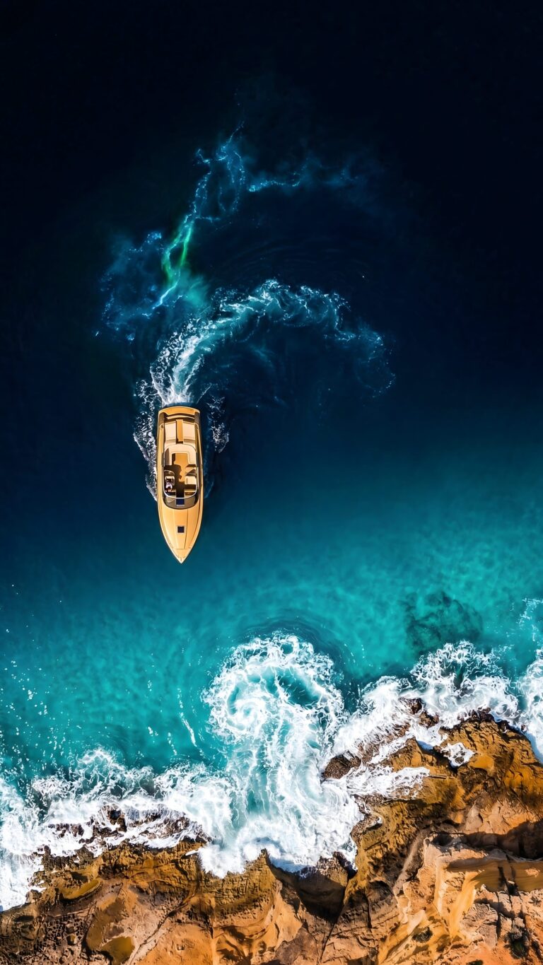 Aerial view of a golden luxury speedboat navigating through deep blue coastal waters near rocky cliffs