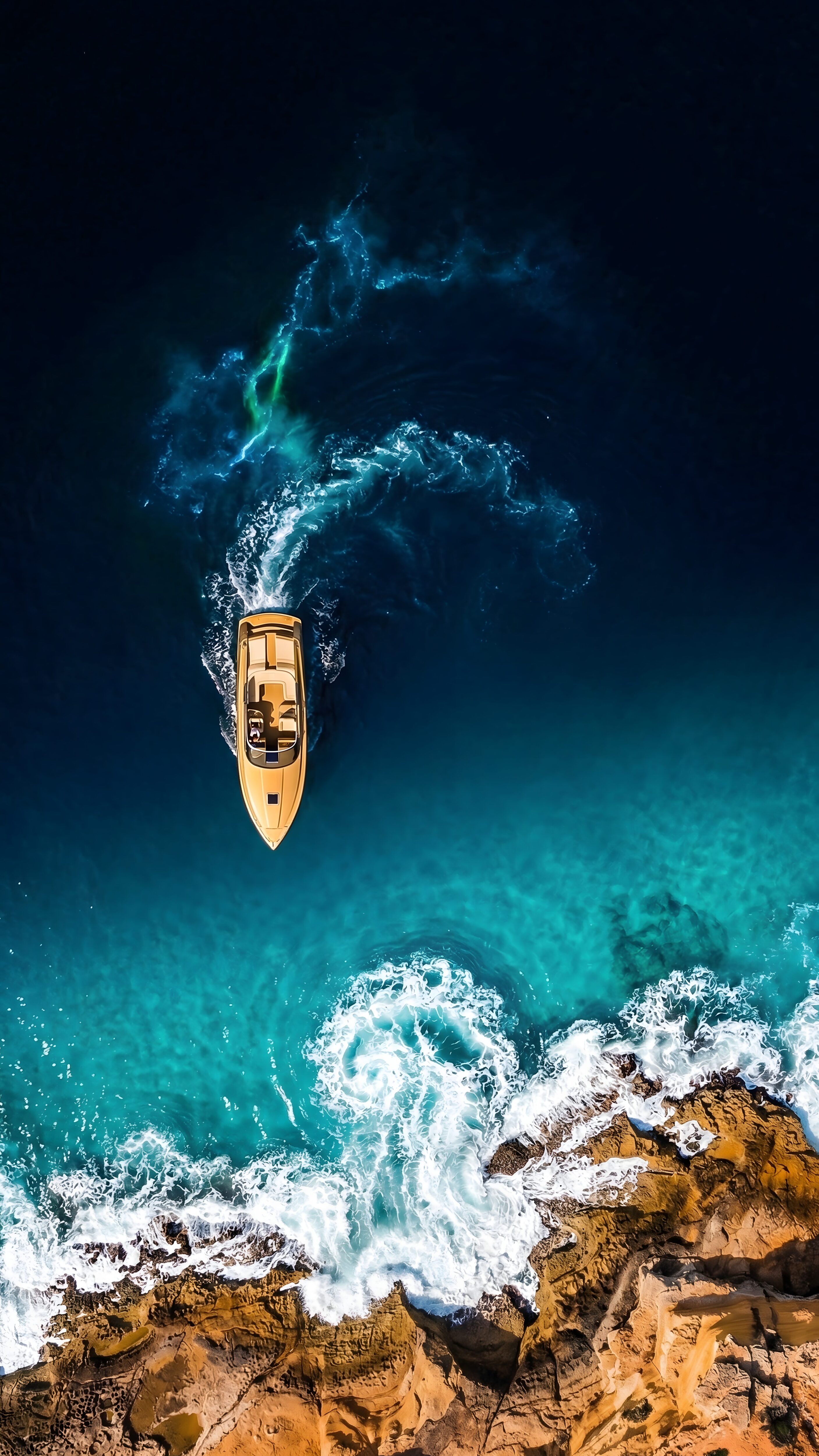 Aerial view of a golden luxury speedboat navigating through deep blue coastal waters near rocky cliffs
