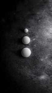 Three smooth white spheres stacked vertically by size on a dark, textured cratered lunar surface.