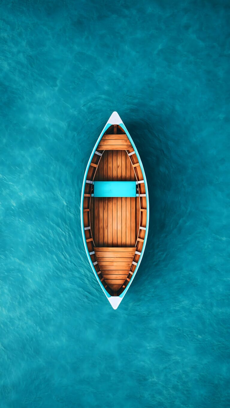 A high-angle, top-down view of an empty wooden boat floating peacefully on bright turquoise ocean water.