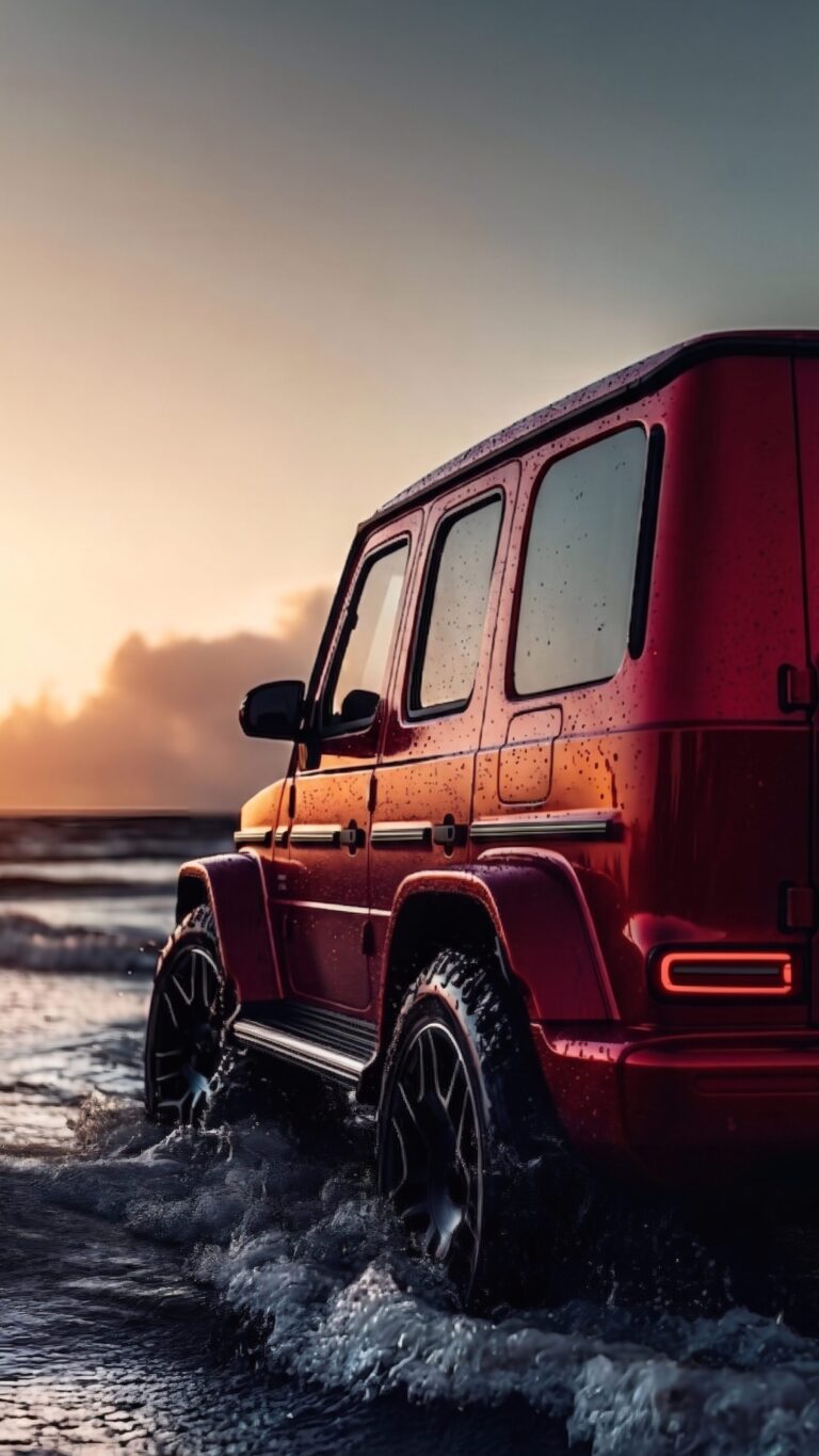 A bright red Mercedes-Benz G-Wagon driving through splashing ocean waves during a vibrant golden hour sunset.