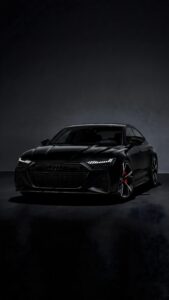 Sleek all-black Audi sports car with glowing LED headlights and red brake calipers in a moody dark studio setting.
