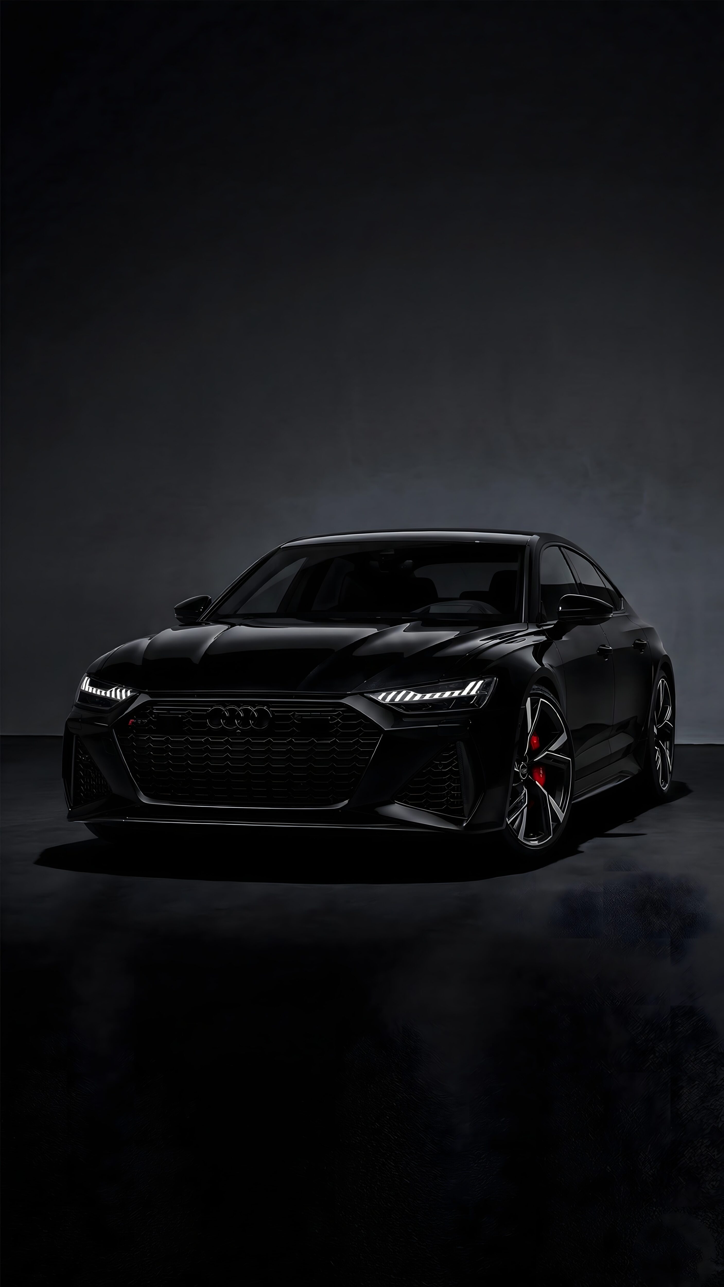 Sleek all-black Audi sports car with glowing LED headlights and red brake calipers in a moody dark studio setting.