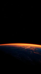 A breathtaking vertical view of Earth from space with a glowing orange atmospheric sunrise against a pitch-black starry sky.